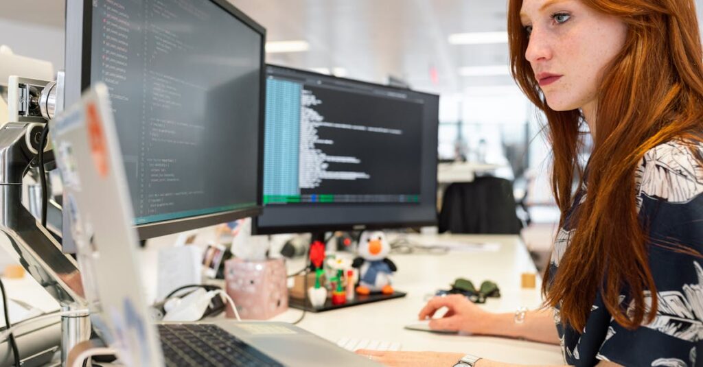 A focused female software engineer coding on dual monitors in a modern office.